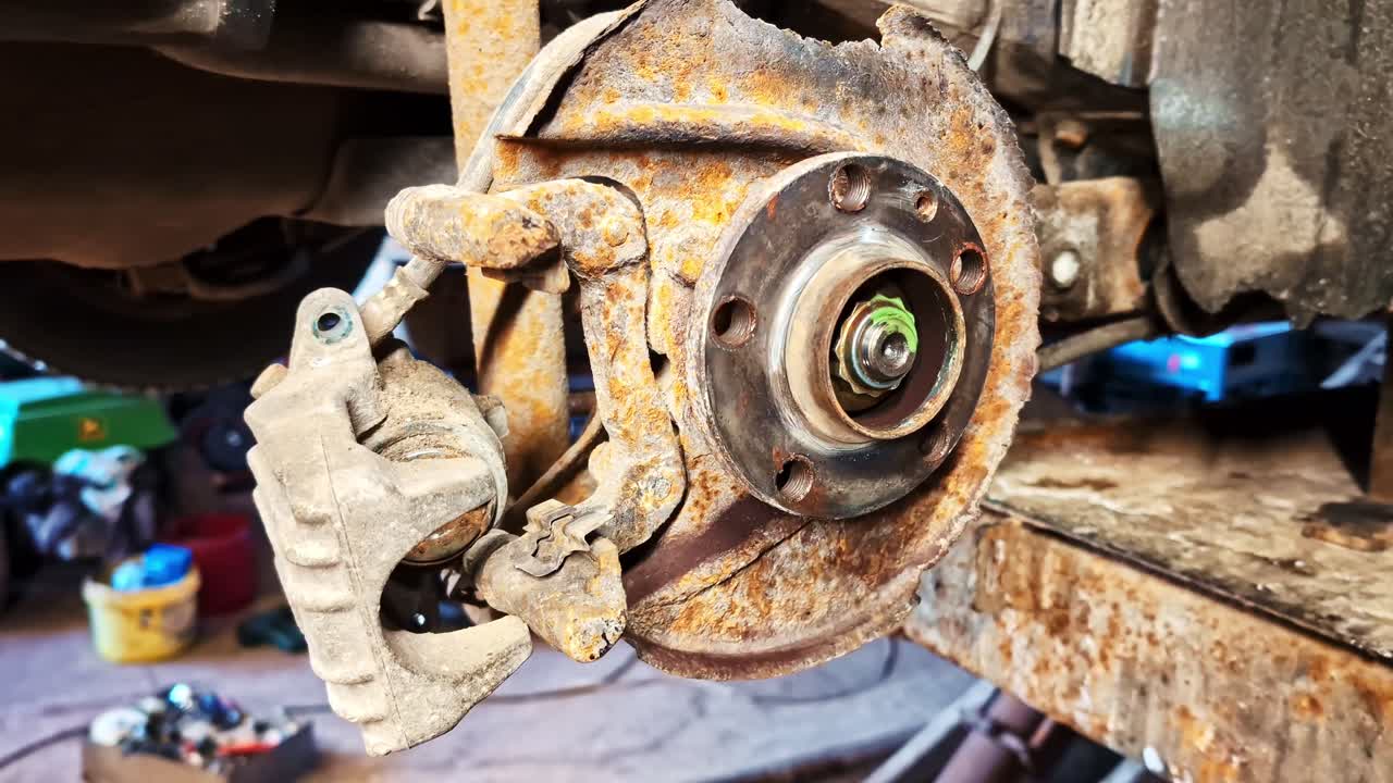 Disco de freio de carro e pinça enferrujados mostrando corrosão e necessidade de substituição.
