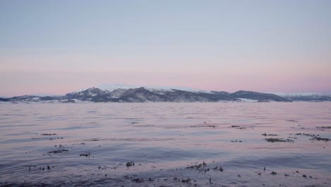 Wintersonnenuntergang-über-Plätscherndem-Fjord-Mit-Schneebedeckten-Bergen-Im-Hintergrund