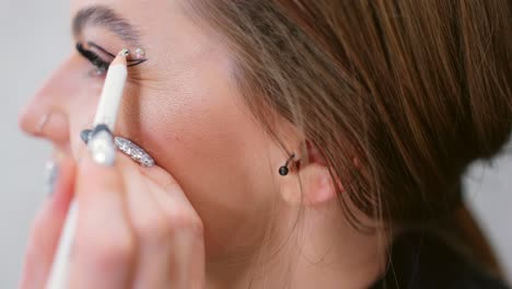 close-up of a woman applying creative eye makeup with eyeliner and decorative rhinestones