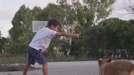 Kaukasischer-Kleinkindjunge,-Wirft-Einen-Plastikspielzeugstock-Auf-Seinen-Hund-Im-Freien,-Zeitlupe