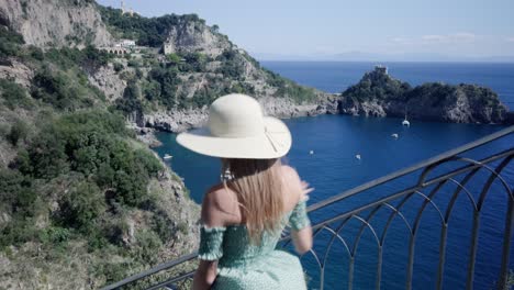 beautiful woman walking down the stairs overlooking mediterranean seascape and rocky cliffs in conca dei marini, amalfi coast, italy