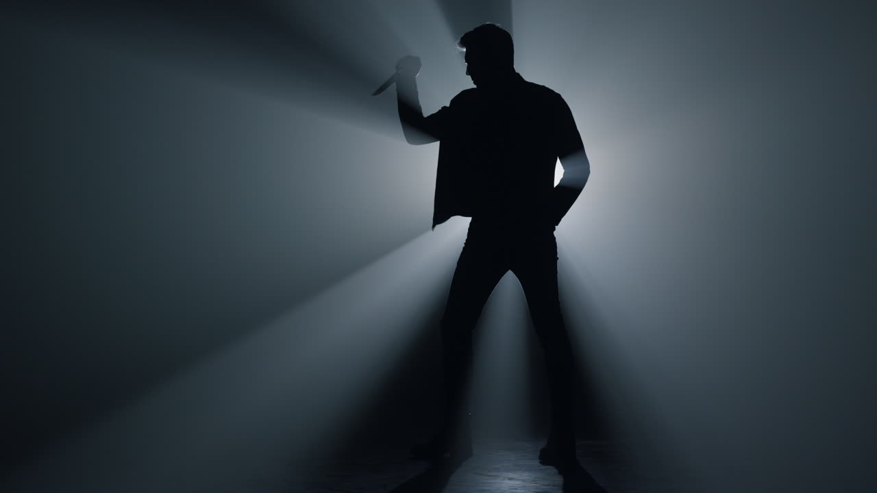 Silhouette di uomo che impugna un coltello nell'oscurità. Criminale in piedi con un pugnale.