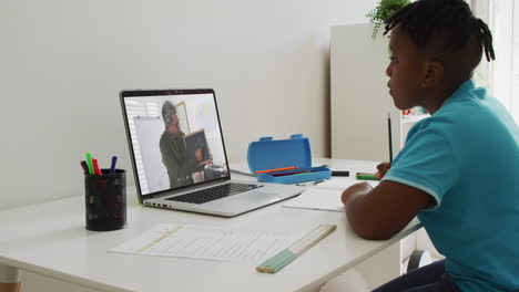 niño afroamericano sentado en un escritorio usando una computadora portátil teniendo una lección escolar en línea