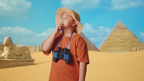 asian boy with a hat and binoculars thinking about something and looking around while traveling in giza pyramid. boy researcher, travel tourism adventure concept