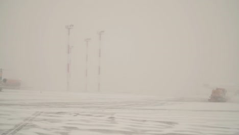 orange snow plows are cleaning snow from the airport landing path at foggy, snowy day