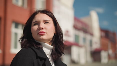 close-up of a confident young woman turning to look ahead, sunlight highlighting her face and subtle nose ring, with blurred buildings in the background