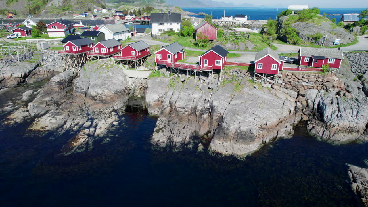 Innflyvende opptak over vakre røde hus i tettstedet Hamnøy med fjell i landskapet
