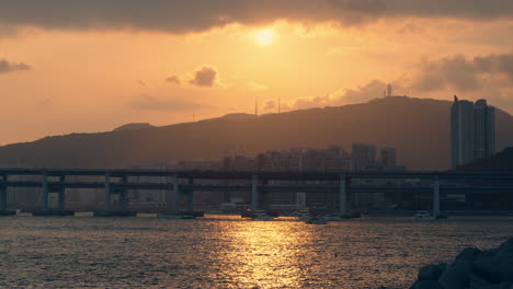 sun setting over hwangnyeongsan beacon mound with view of gwangan bridge during golden sunset in busan, group of tour yachts and boats in silhouette