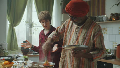 indian chef stirring food and speaking with young woman during cooking class