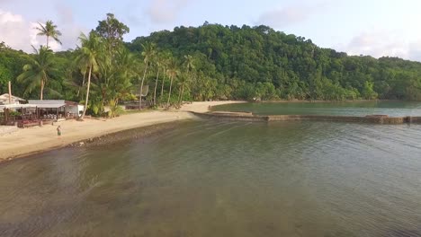 drone dolly shot of small tropical beach with kayak and palm trees and a resort in thailand