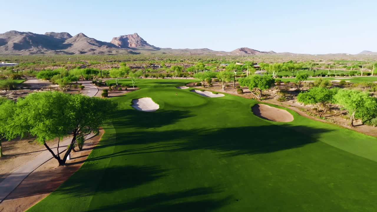 Drone push-in over a desert golf fairway with sand bunkers, lush grass, and distant mountain views