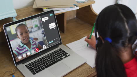 schoolgirl using laptop for online lesson at home, with girl talking and web chat on screen