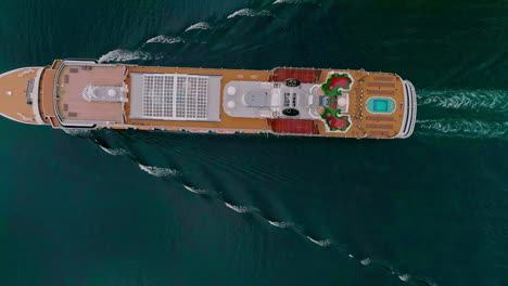 Aerial-drone-top-shot-over-a-giant-cruise-ship-in-motion-along-Norwegian-Fjord-in-Flam,-Norway-on-a-cloudy-day