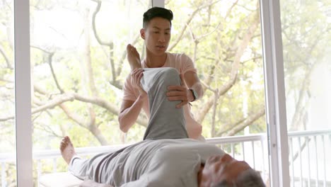 diverse male physiotherapist advising and senior male patient stretching, in slow motion