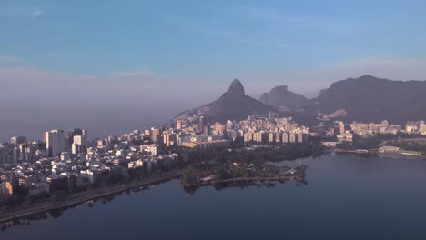 acercamiento aéreo sobre el lago de la ciudad hacia la isla y el club caiçaras en ipanema en primer plano y leblon y la montaña dos hermanos en el fondo al amanecer temprano