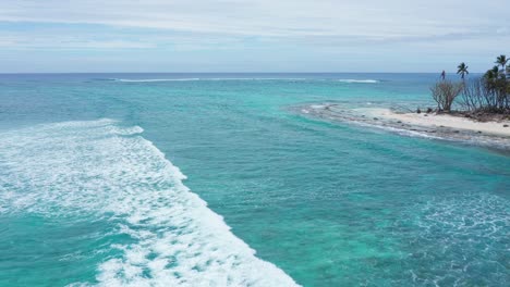 drone shot of turquoise sea waves breaking on coast of small tropical island with white sand