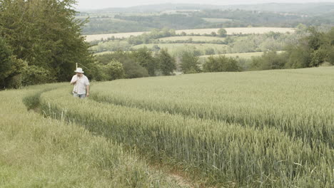 Farmer-in-field-going-home-after-work-with-scythe-on-back,-cinematic-slowmo-shot