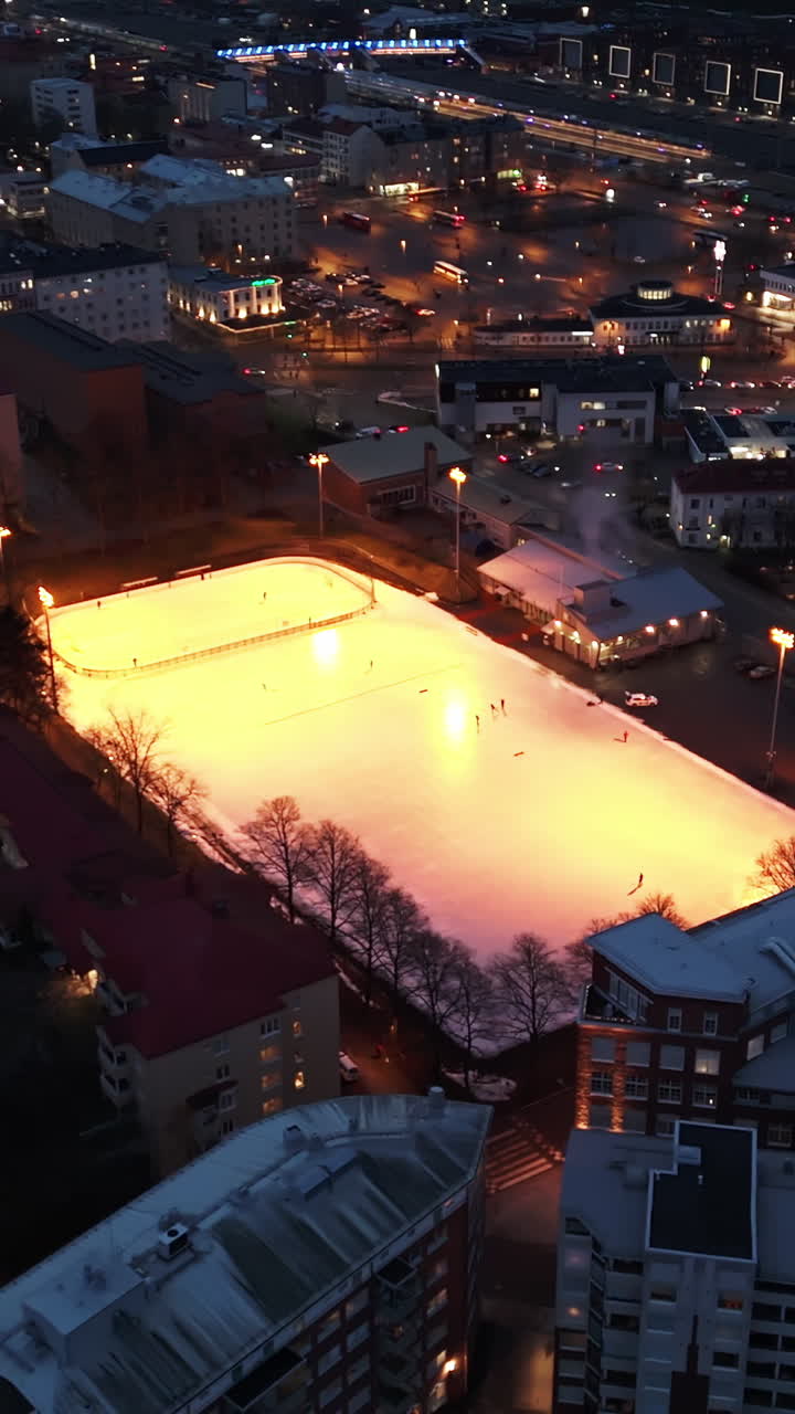 Vertical drone shot circling a illuminated ice hockey rink, dark evening in Turku