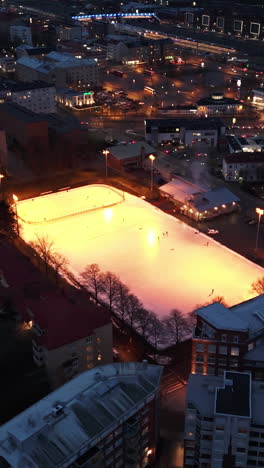vertical drone shot circling a illuminated ice hockey rink, dark evening in turku