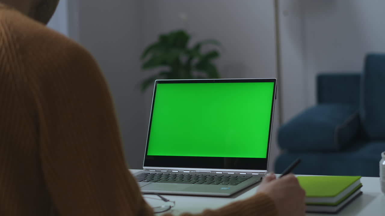 portátil con pantalla verde en la mesa de trabajo en la oficina de casa vista a través del hombro del hombre trabajo remoto y videoconferencia independiente