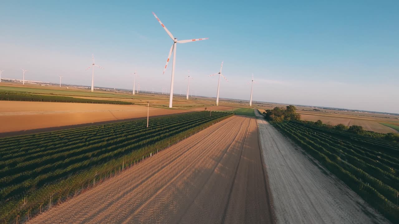 Aerial shot of vineyards and wind turbines in a field. Flying with a drone towards wind turbines in the background.