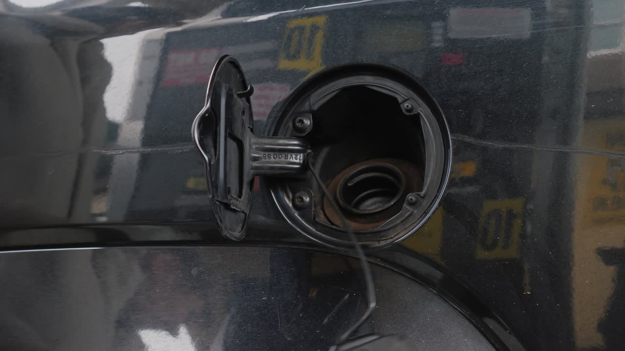 A woman in winter clothes runs her car. Opens the fuel tank cap and inserts the refueling gun