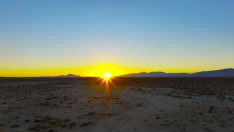 sunset with the golden fiery orb of the sun just above the mountainous horizon in the mojave desert - push forward