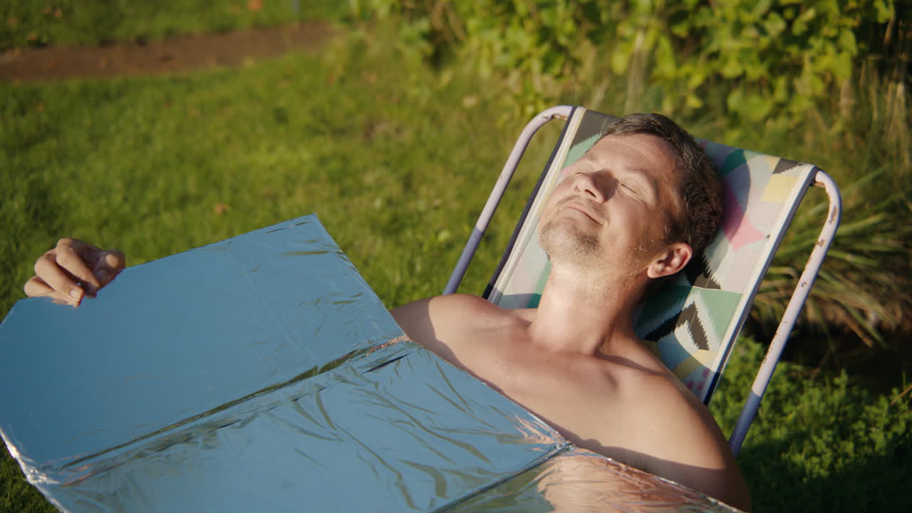Man sunbathing with a solar concentrator in a garden