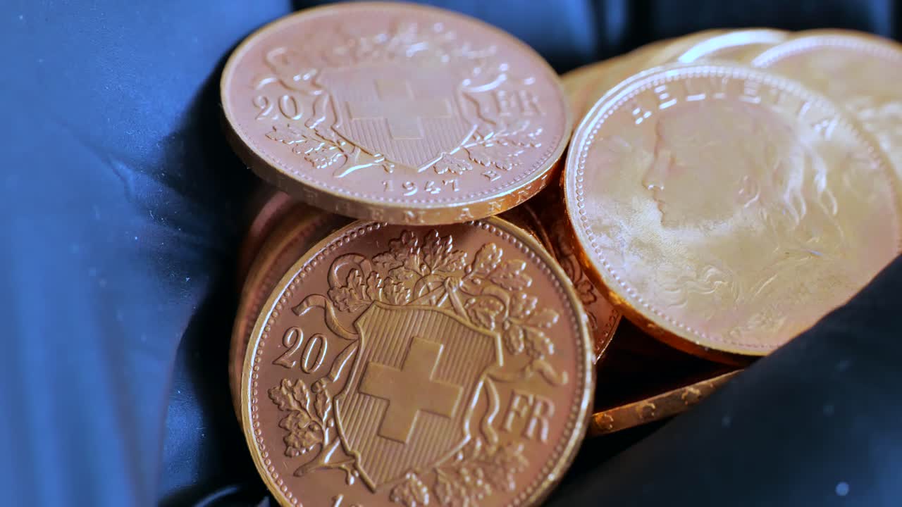 Handheld close up of many golden 20 vreneli francs lighting by sunlight. Helvetia and swiss cross depicted.