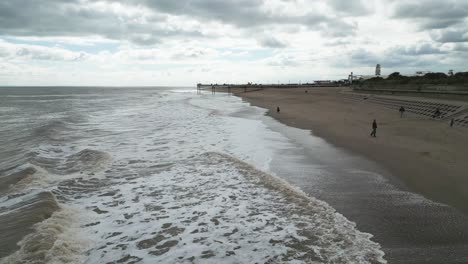 Typical-English-seaside-resort,-shot-using-a-drone,-giving-a-high-aerial-viewpoint-showing-a-wide-expanse-of-sandy-beach-with-a-pier-and-crashing-waves-7