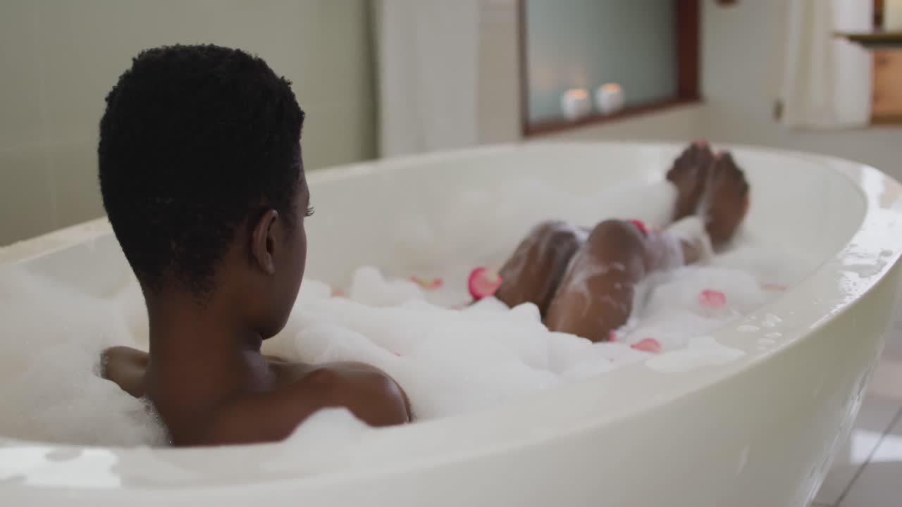 Back view of african american attractive woman taking bath with foam and rose petals