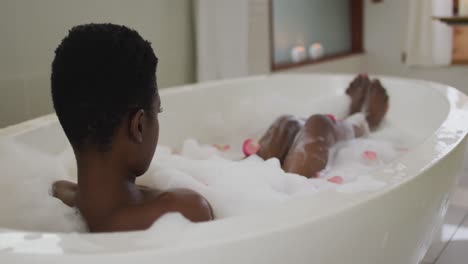 Back-view-of-african-american-attractive-woman-taking-bath-with-foam-and-rose-petals