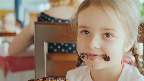 una niña traviesa con la cara manchada de chocolate sonríe al retrato de la cámara