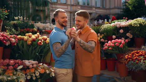 a romantic gay couple smiling and holding hands in a vibrant flower market