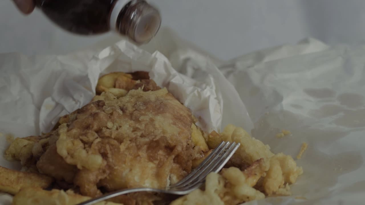 Hand pouring vinegar on fish and chips close up shot