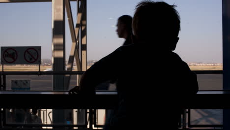 Kleiner-Junge,-Der-Durch-Das-Fenster-Im-Flughafen-Schaut