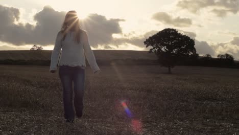 woman walking across farm land field of oats after harvest in sunshine