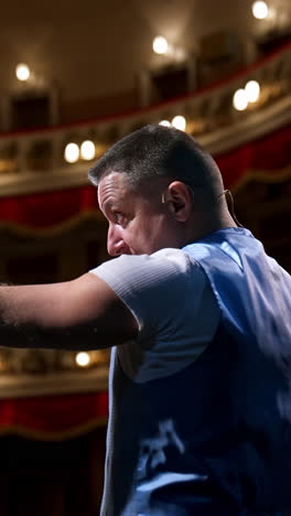 Presenter in front of empty theatre hall with red velvet chairs. Actor is standing on stage and talking with gestures before the performance. Vertical video