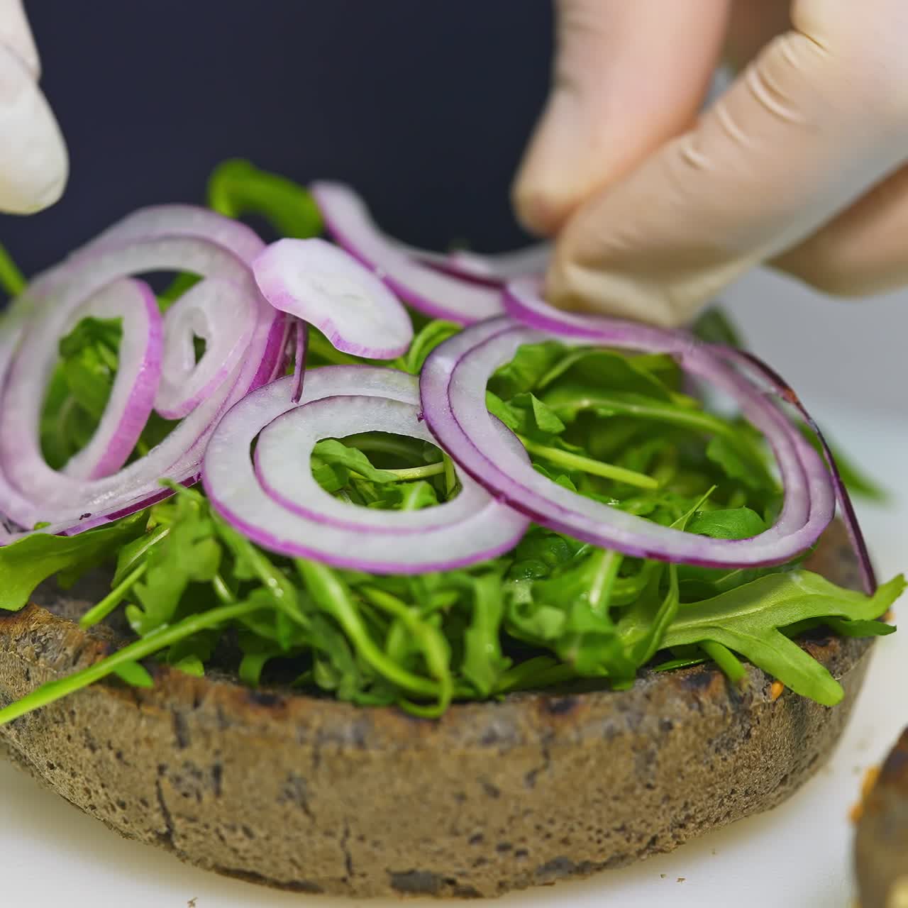 Hamburger ingredients assembling a delicious burger. Side view. Unrecognizible chef in white gloves finishes dish. Selective focus