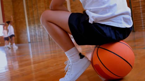 Kaukasisches-Schulmädchen-Im-Unteren-Bereich,-Das-Auf-Basketball-Auf-Dem-Basketballplatz-In-Der-Schule-Sitzt,-4K