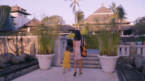 mother and daughter walking on the pathway through the pools of intercontinental bali resort, indonesia