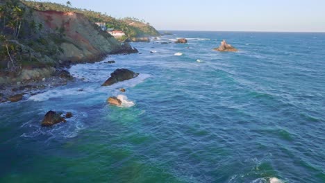 Aerial-flight-along-coastline-of-samana-with-rocks-in-water-and-luxury-villa-in-bay-during-sunset---whale-watching-spot