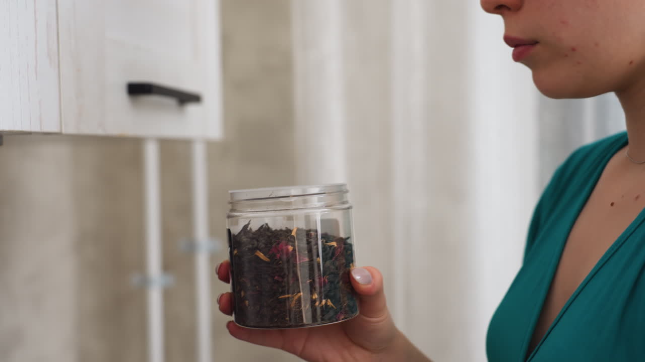 Caucasian Woman Placing Tea Jar Cabinet Careful Hands Shelve Sealed Jar Then Lift To Sniff Aroma, Thoughtful Selection Of Blend In Tidy Kitchen, Quiet Sensory Ritual And Organized Storage