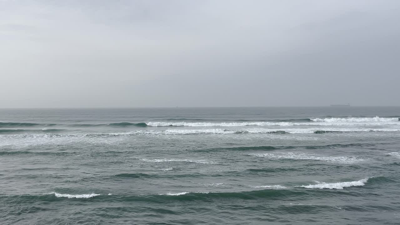 A peaceful scene of the Portuguese coastline, where gentle waves roll over the ocean, creating a serene atmosphere. The muted sky and calm waters reflect the tranquil beauty of the seascape.