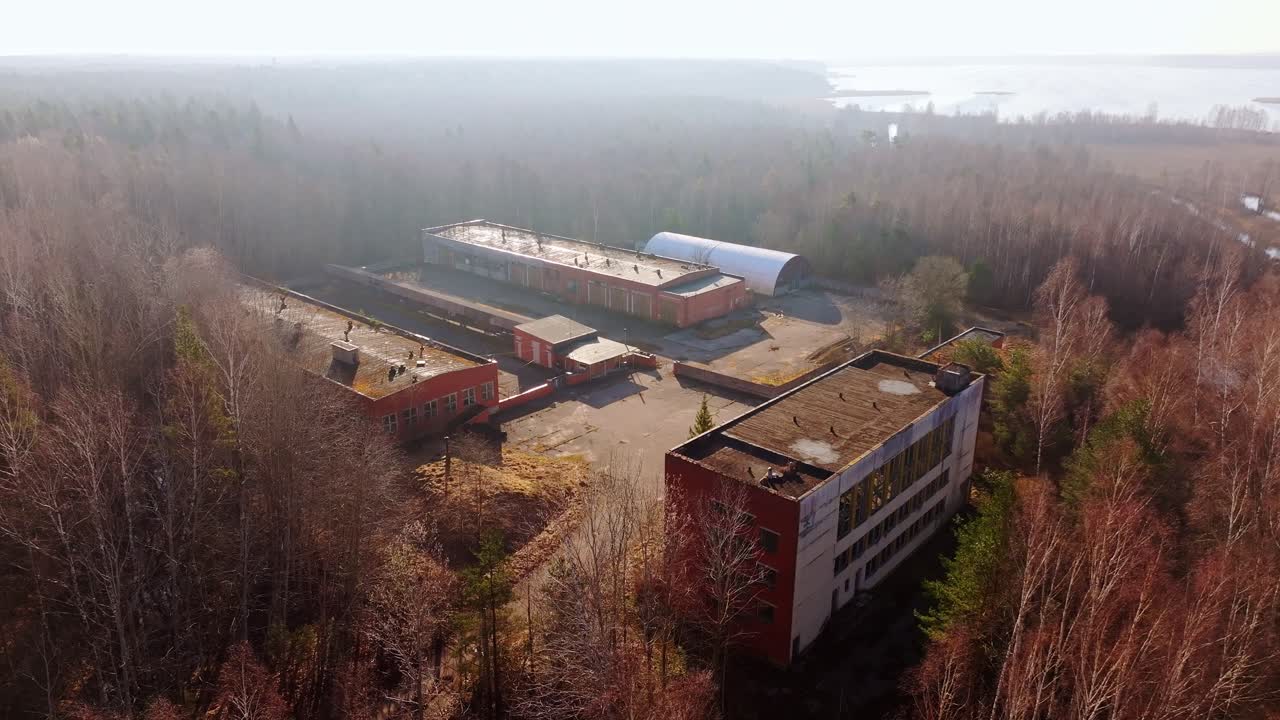 Derelict industrial area surrounded by trees, distant lake under spring sunlight