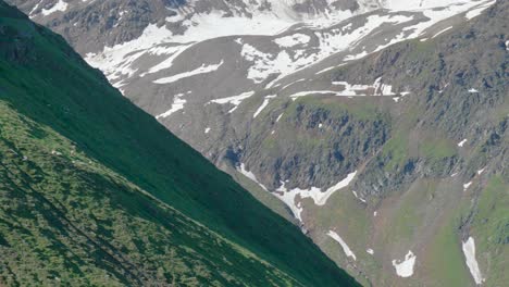 Green-foliage-and-melting-snow-during-Spring-in-Swiss-Alps-valley,-panning-drone