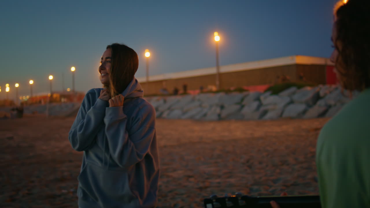 십대 여성이 저녁 해변에서 춤을 춘다. 알려지지 않은 남성 음악가 기타를 연주하는 황혼