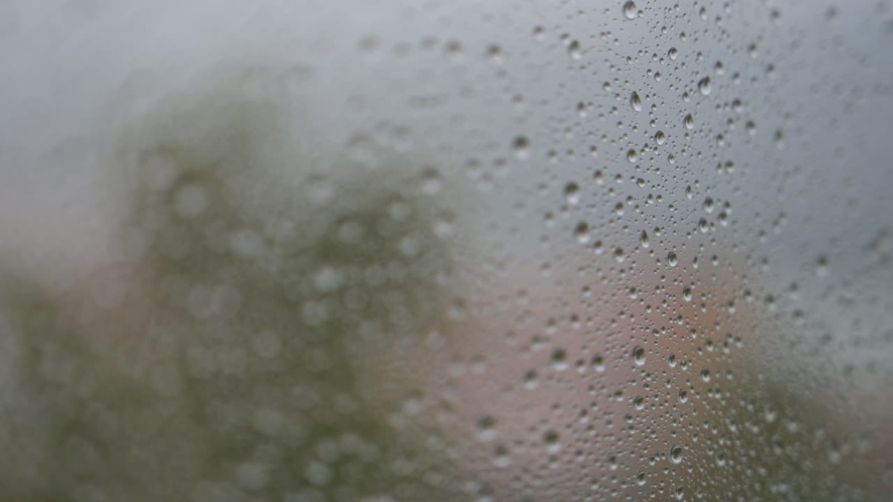 During a gloomy and overcast day, a narrow focus view of rainy glass as rain drops are seen on a window