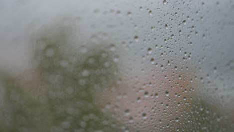 during a gloomy and overcast day, a narrow focus view of rainy glass as rain drops are seen on a window