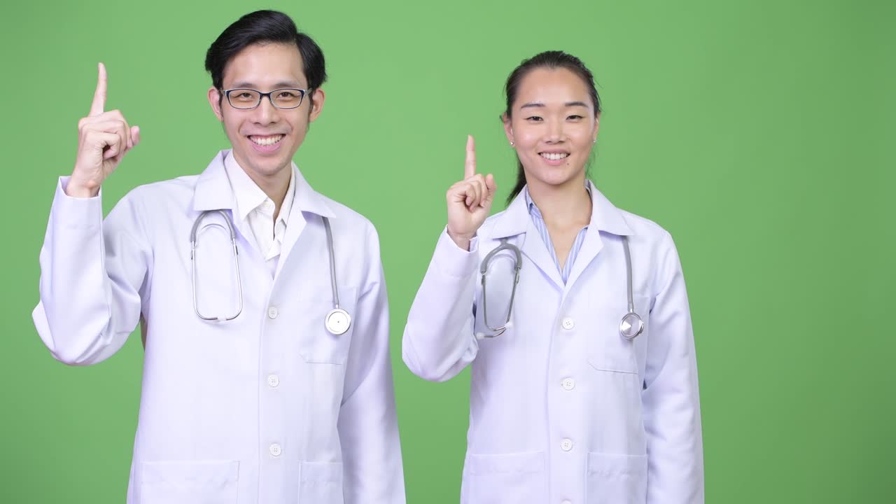 Young Asian couple doctors pointing up together